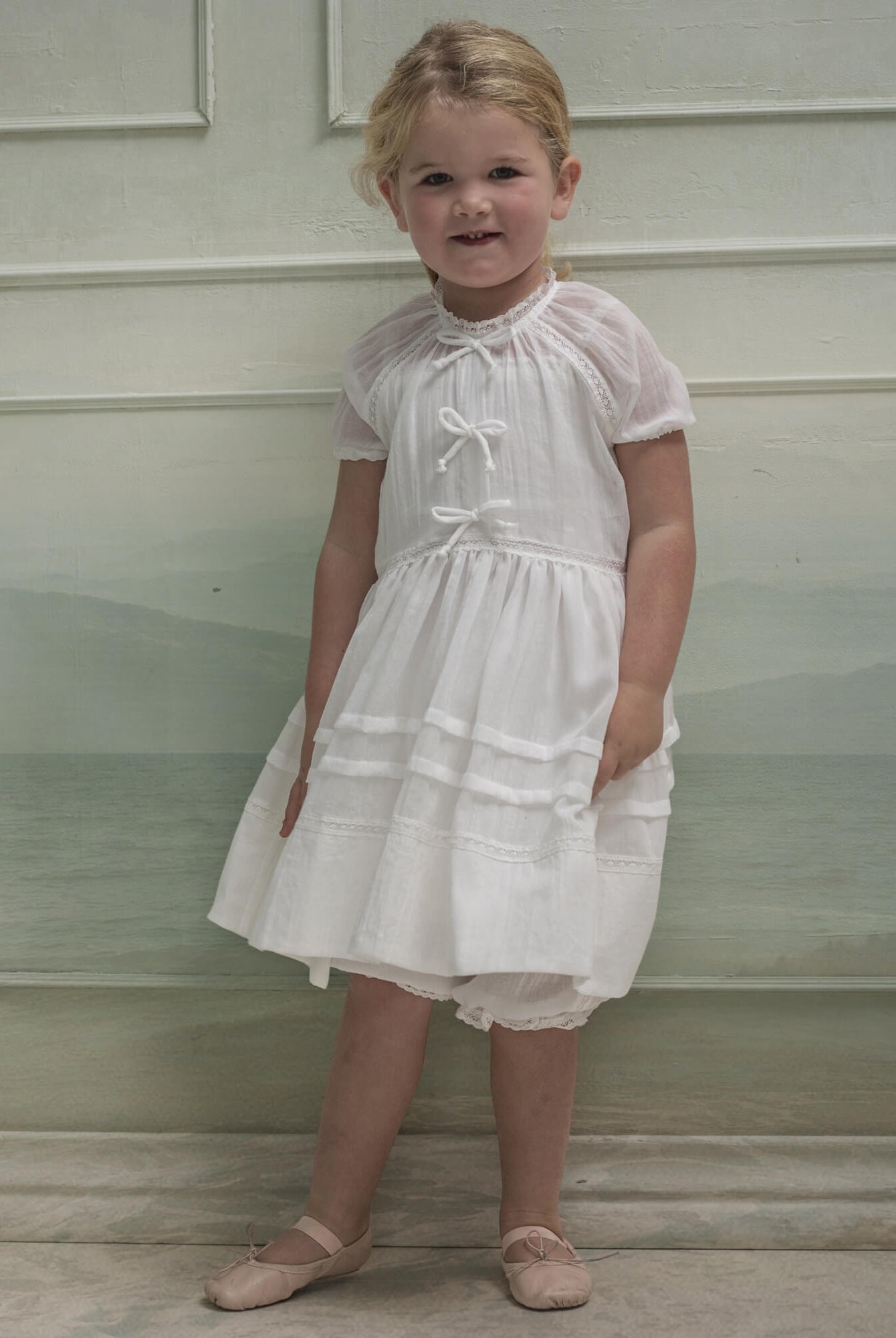 Vestido en blanco roto con lazitos en el pecho y encajes, falda con lorzas y pololos a juego Cosmosophie