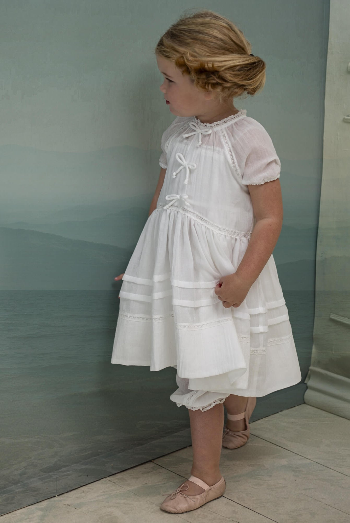 Vestido en blanco roto con lazitos en el pecho y encajes, falda con lorzas y pololos a juego Cosmosophie