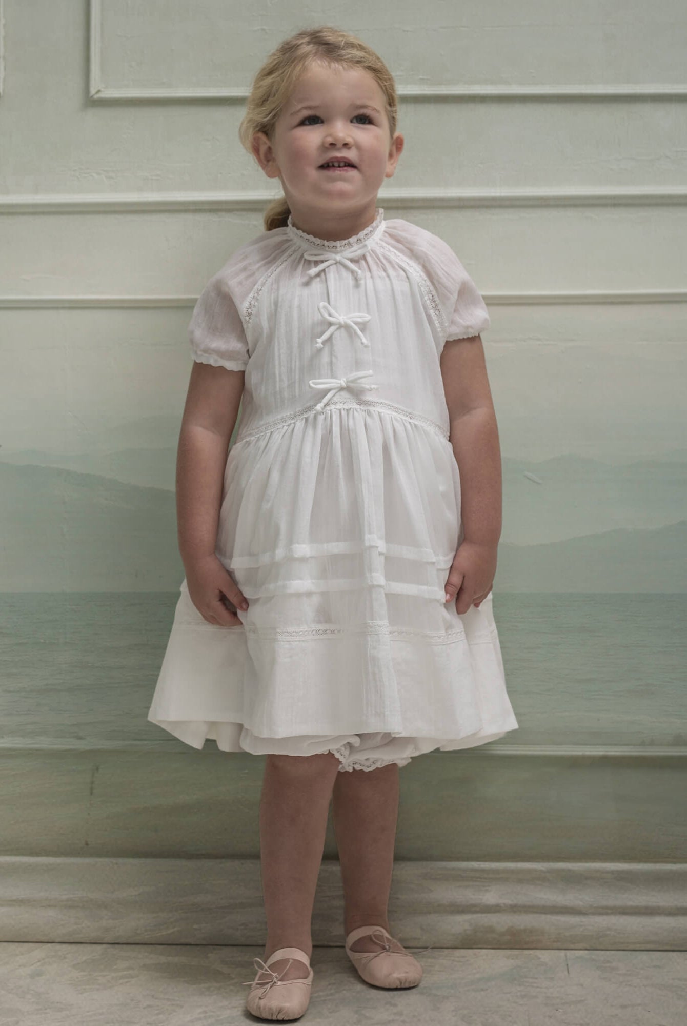 Vestido en blanco roto con lazitos en el pecho y encajes, falda con lorzas y pololos a juego Cosmosophie