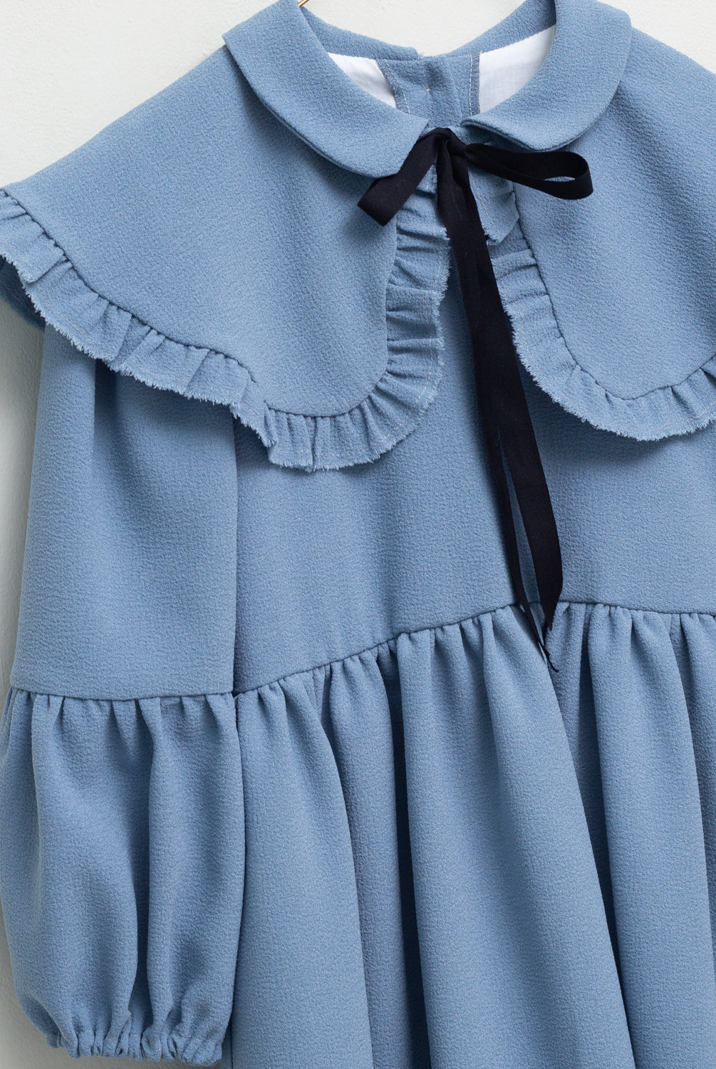 Vestido azul celeste con capita con volantes y lazo negro