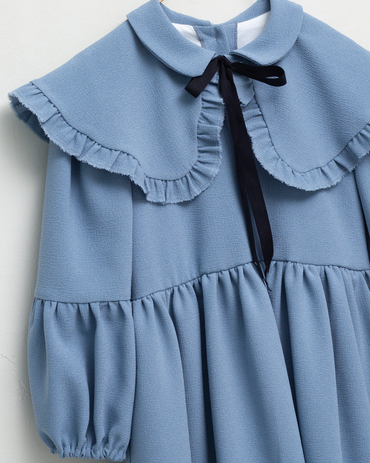 Vestido azul celeste con capita con volantes y lazo negro