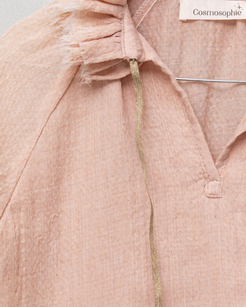 Blusa de mujer rosa con efecto jacquard, cuello de volantes deshilachados y cordones dorados. Diseño femenino y especial.