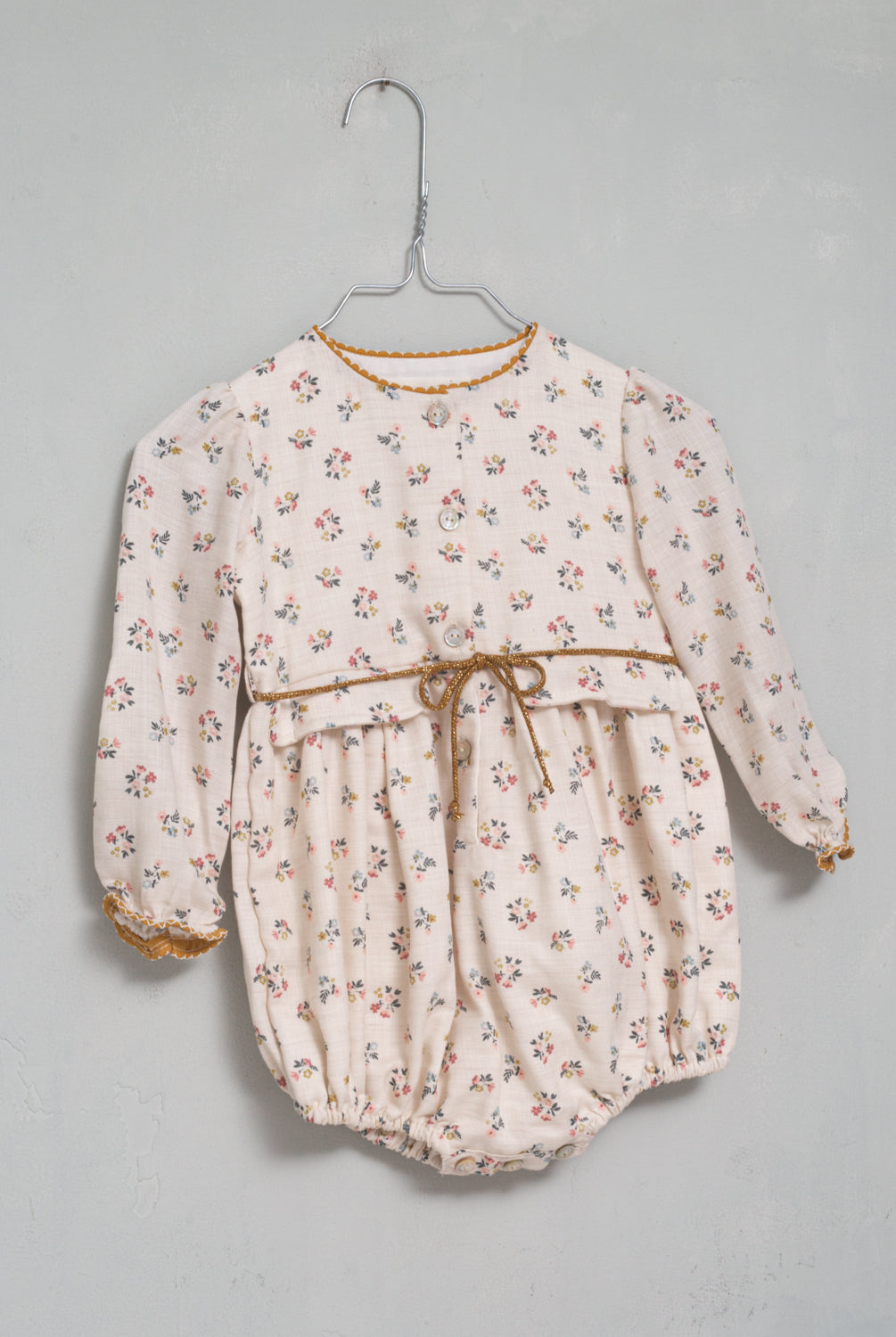 Your baby will look beautiful in this floral print romper in blue, pink and mustard on an ecru background. You'll love the contrasting detail on the neck, its decorative pockets and its tie detail at the waist. Front button closure and between legs. Elasticated cuffs for greater comfort.