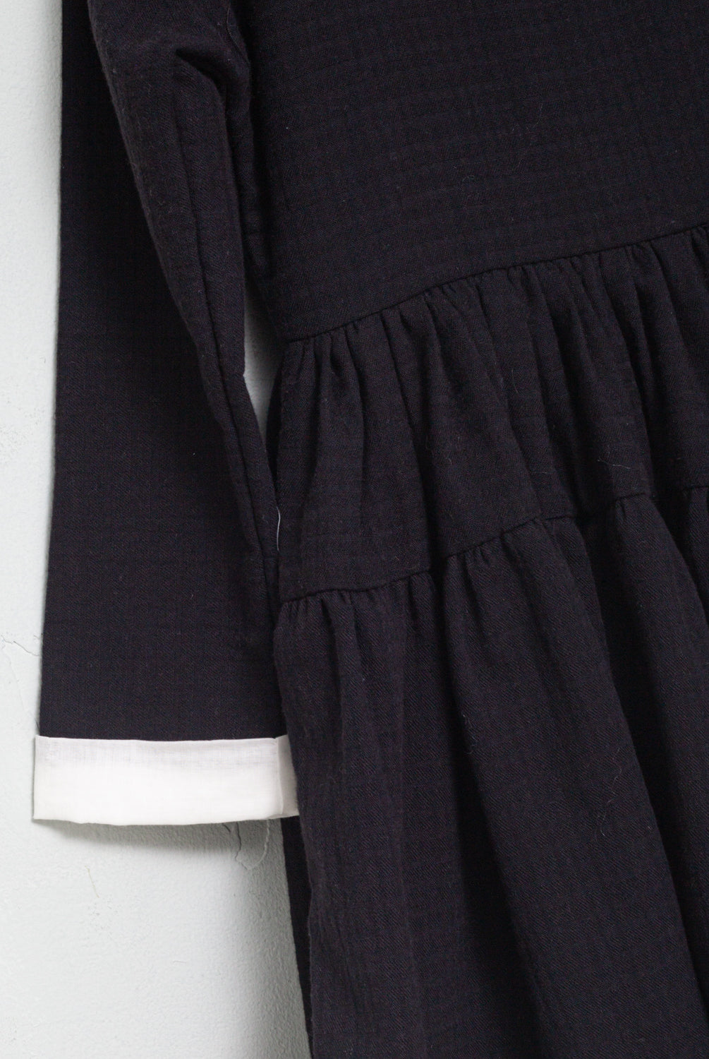 One of the most romantic dresses in the collection. Made of black cotton with gingham jacquard. You'll love its huge, gathered collar in off-white muslin. Small bow detail on the neck in an ecru and gold tone. The sleeve has a contrasting off-white muslin detail. Double flounce skirt. It buttons in the back.