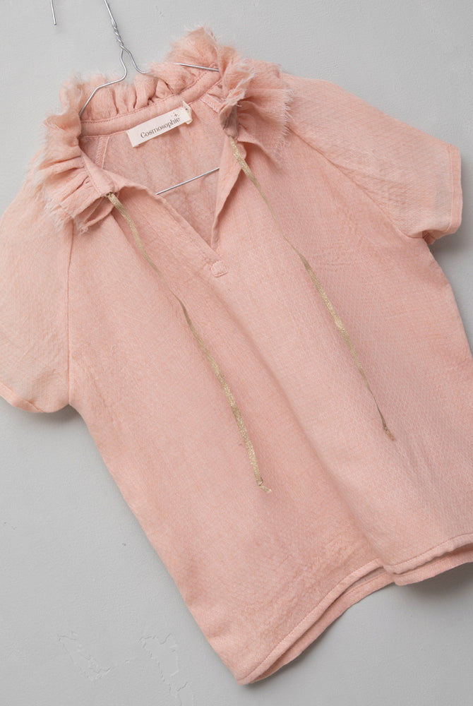 Blusa de mujer rosa con efecto jacquard, cuello de volantes deshilachados y cordones dorados. Diseño femenino y especial.