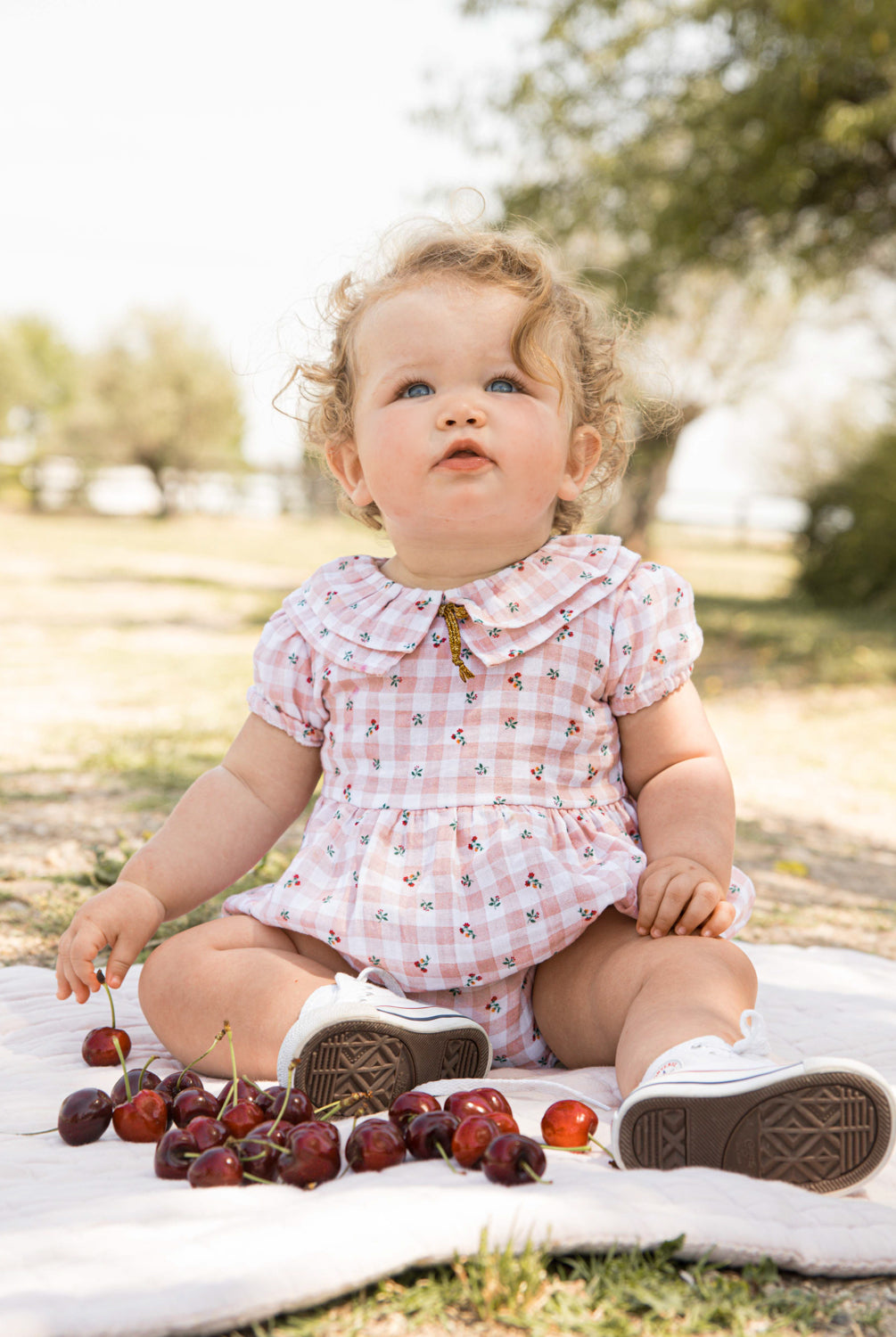 Romper for baby dress in gingham print with flowers. Ruffle neck and gold bow detail. Cosmosophie