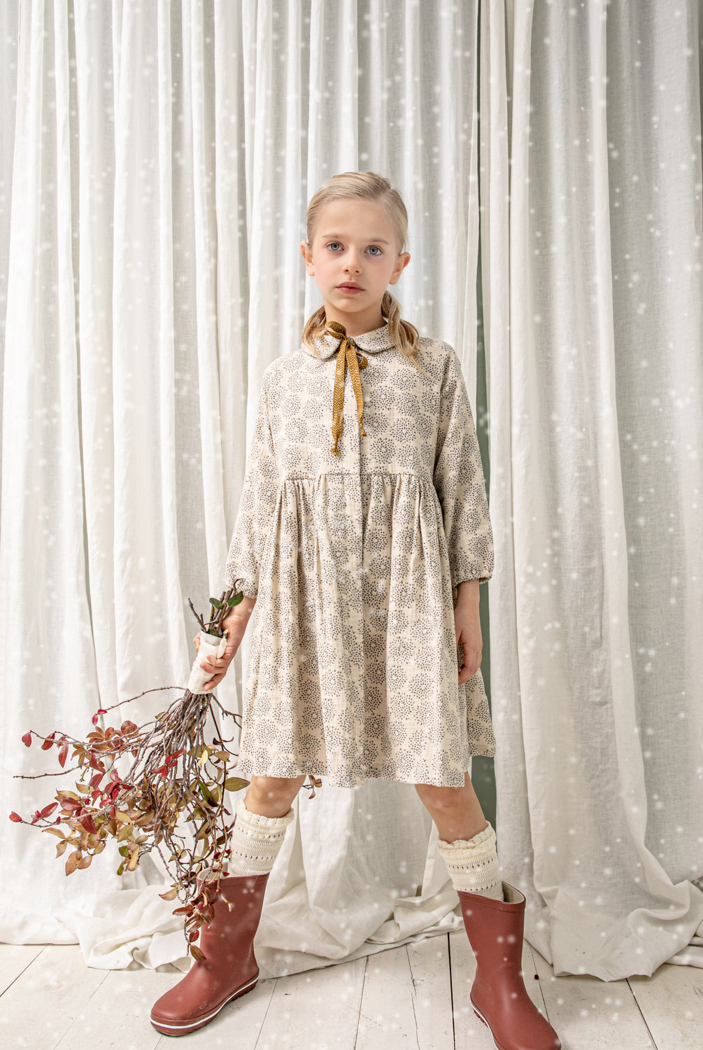 Gemini es un vestido abierto por delante para que puedas usarlo como abrigo. Esta realizado en un tejido de jacquard en color crudo con estampado de dalias en color gris. Los botones estan ocultos bajo una tapeta. Te encantará su manga ranglan y el detalle de lazada dorada en el cuello