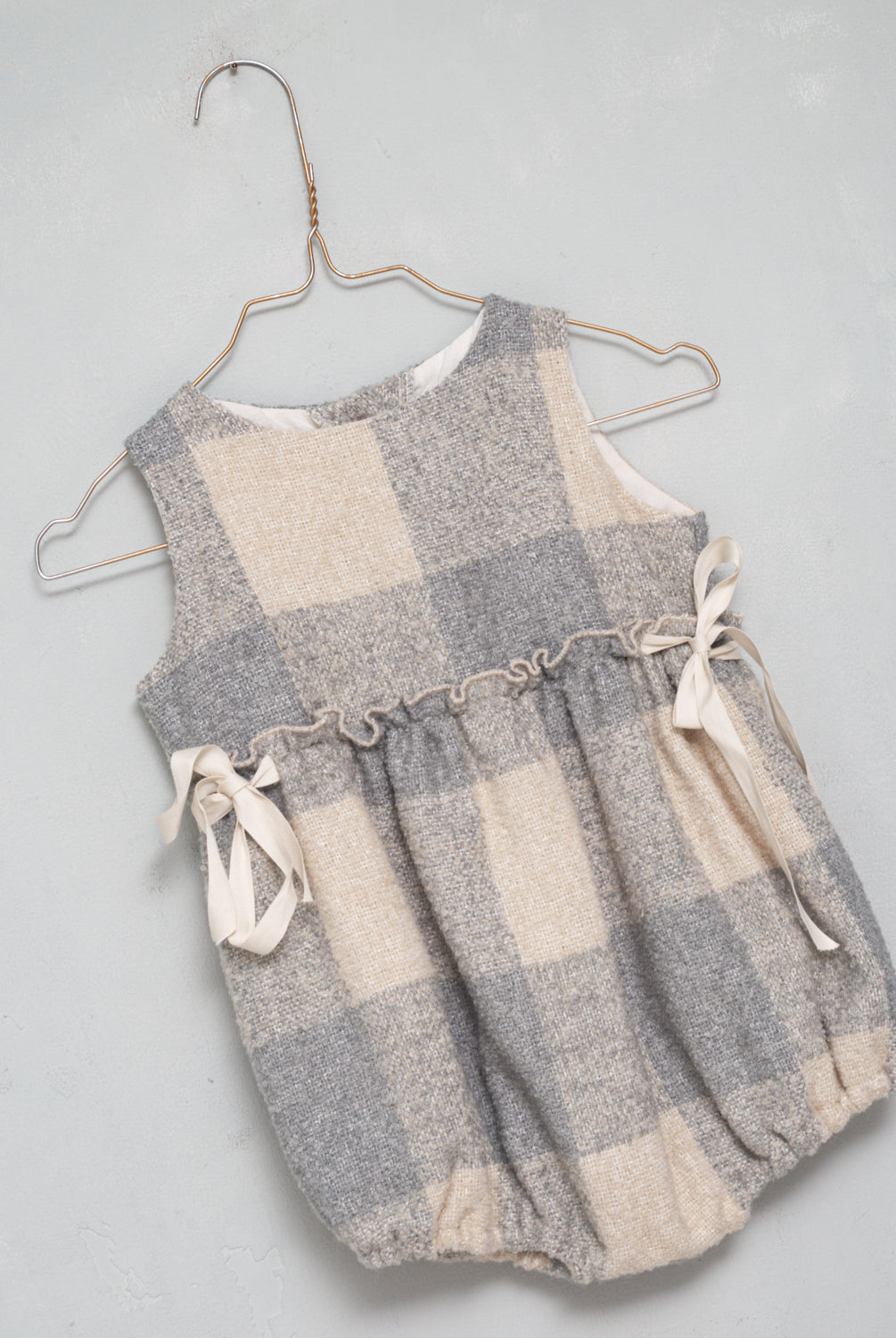 Beautiful pinafore romper in soft oversize gingham fabric in ecru and bluish grey. Perfect to wear with one of our ruffle neck blouses. You will love its bows on the sides.
