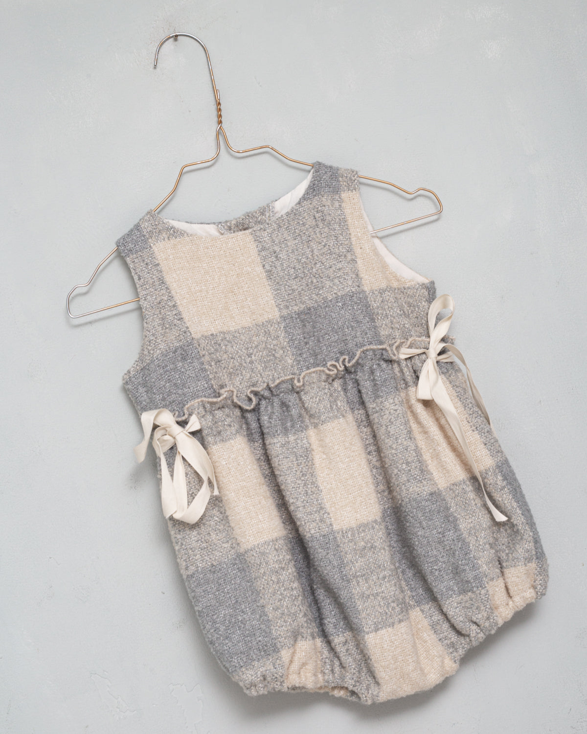Beautiful pinafore romper in soft oversize gingham fabric in ecru and bluish grey. Perfect to wear with one of our ruffle neck blouses. You will love its bows on the sides.