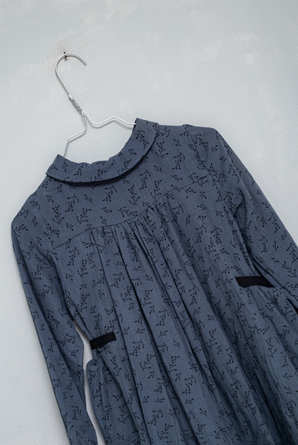 Front button dress with baby collar. You will love its blue double gauze fabric with a print of small black flowers. As details, it has a black ribbon that is tied at the waist.