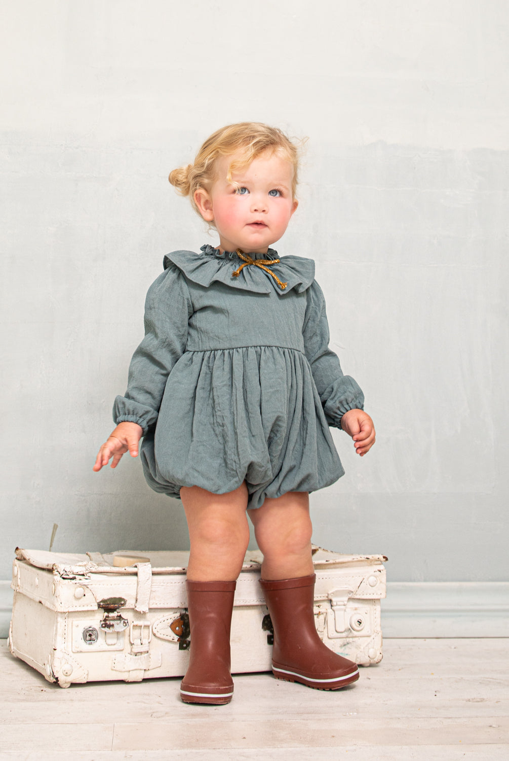 Ranita azul con cuello de volante y lazada en oro para bebe.