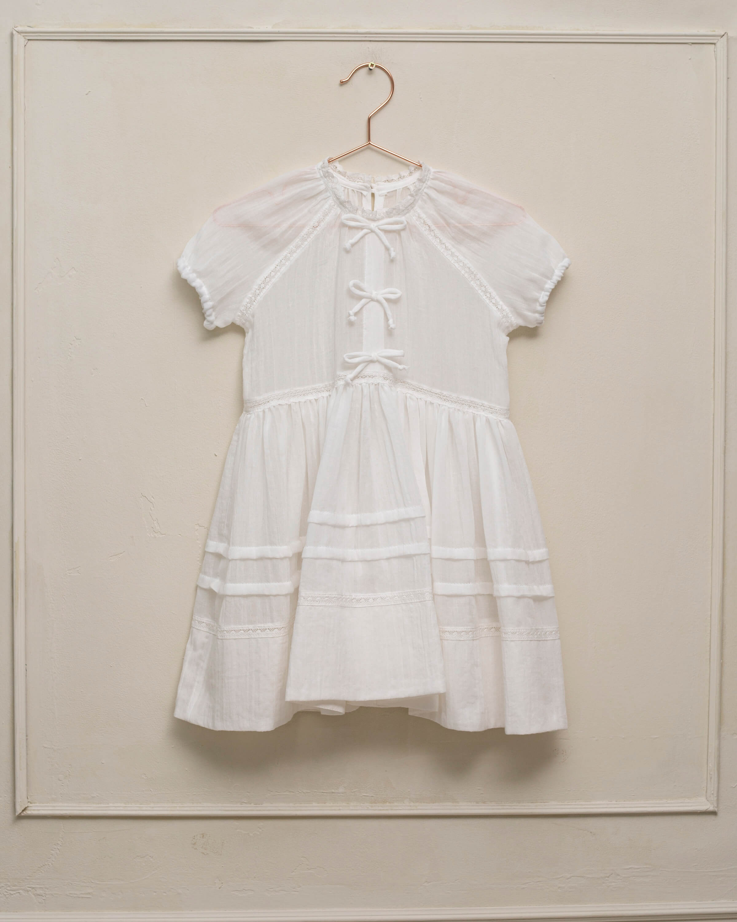 Vestido en blanco roto con lazitos en el pecho y encajes, falda con lorzas y pololos a juego Cosmosophie