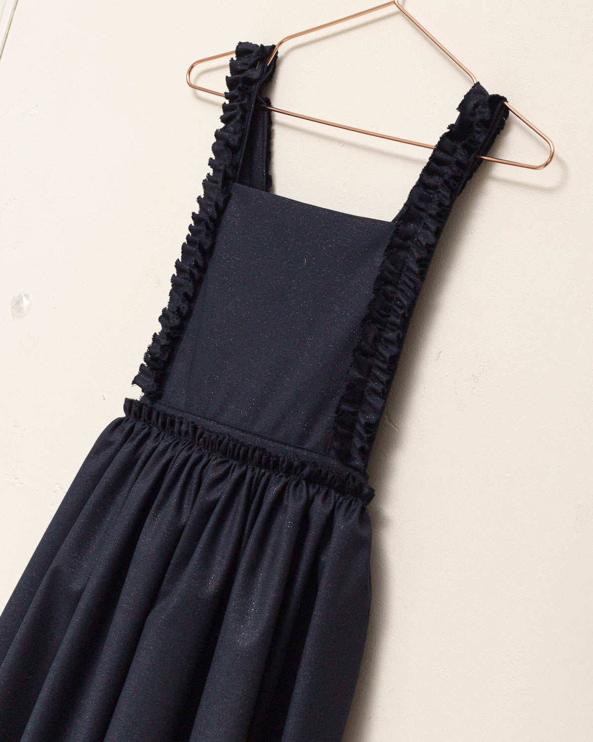 Pichi Pola Glow para niña en lana fría con sutil brillo y tirantes con volantes. Un diseño elegante y femenino, confeccionado en Madrid.