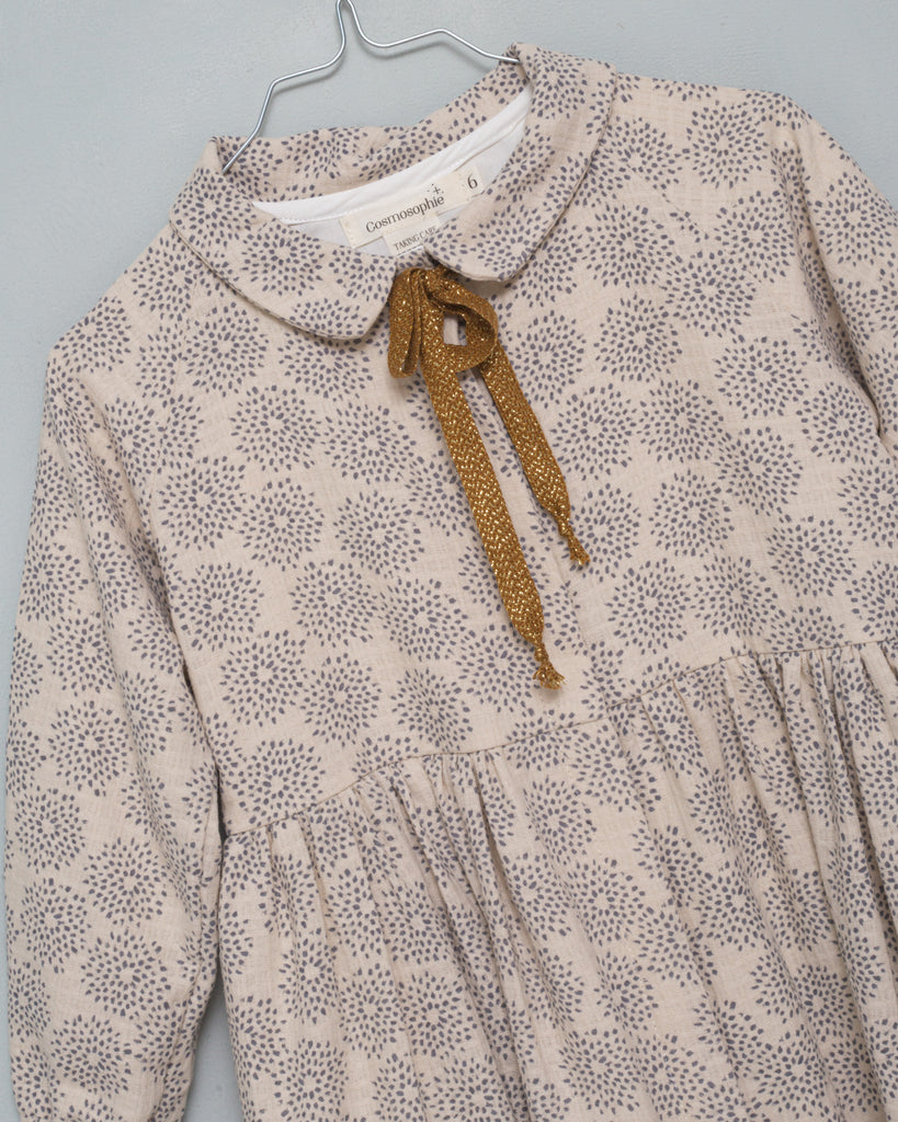 Gemini is an open front dress so you can wear it as a coat. It is made of an ecru jacquard fabric with a gray dahlia print. The buttons are hidden under a placket. You'll love its raglan sleeves and the gold bow detail on the neck.