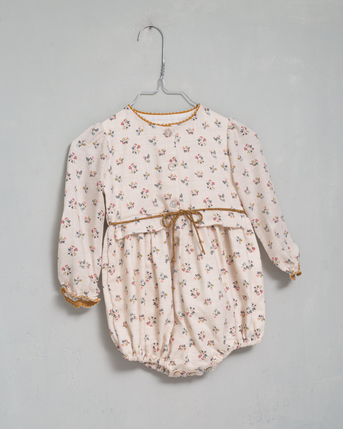 Your baby will look beautiful in this floral print romper in blue, pink and mustard on an ecru background. You'll love the contrasting detail on the neck, its decorative pockets and its tie detail at the waist. Front button closure and between legs. Elasticated cuffs for greater comfort.