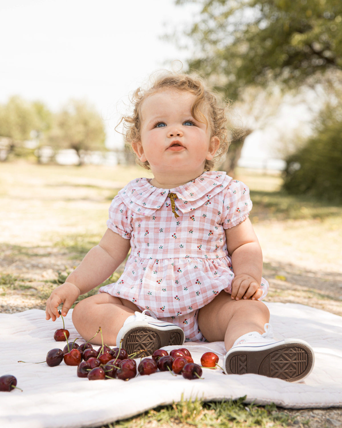 Romper for baby dress in gingham print with flowers. Ruffle neck and gold bow detail. Cosmosophie