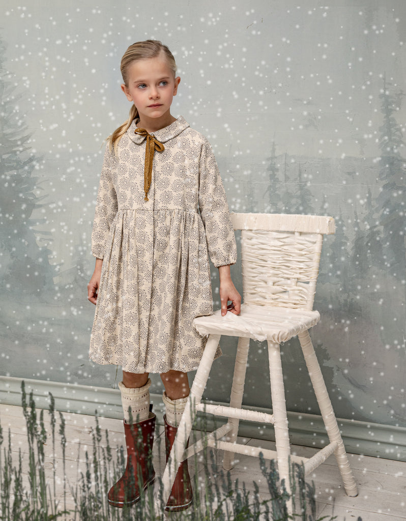 Gemini is an open front dress so you can wear it as a coat. It is made of an ecru jacquard fabric with a gray dahlia print. The buttons are hidden under a placket. You'll love its raglan sleeves and the gold bow detail on the neck.