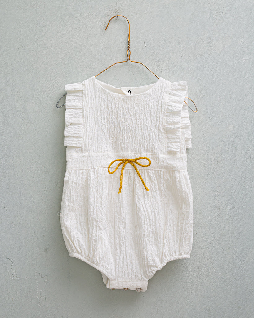 Baby romper in white with ruffled detail and gold bow on waist