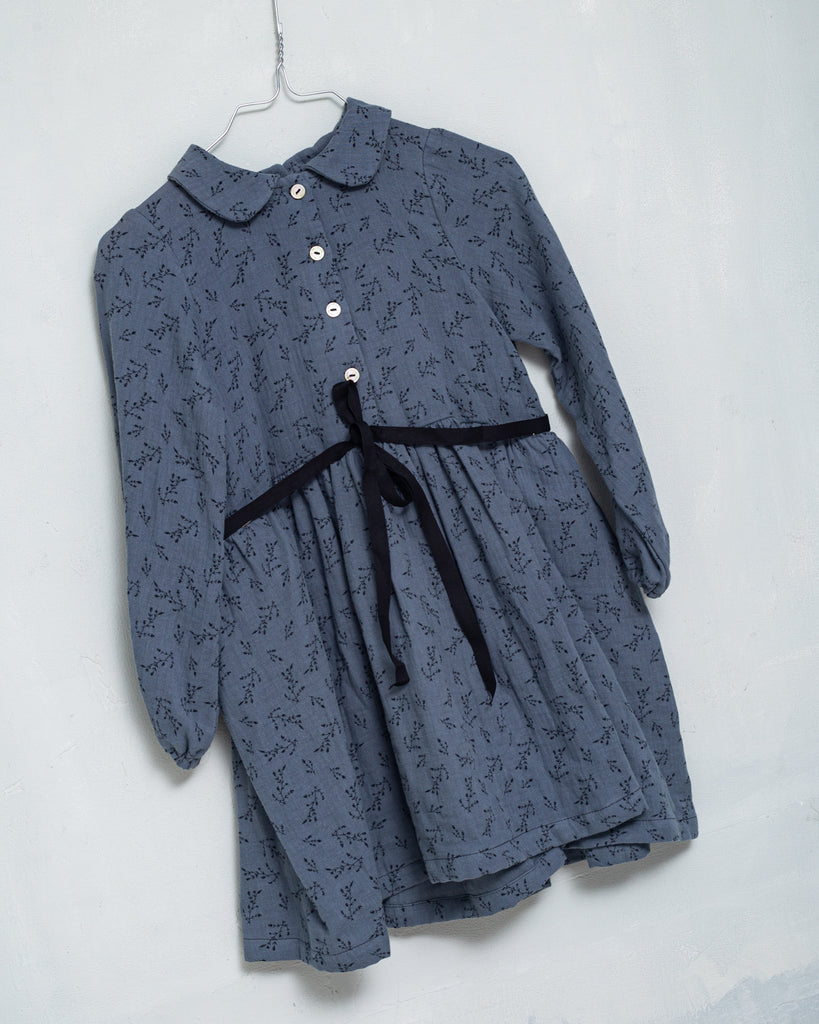 Front button dress with baby collar. You will love its blue double gauze fabric with a print of small black flowers. As details, it has a black ribbon that is tied at the waist.